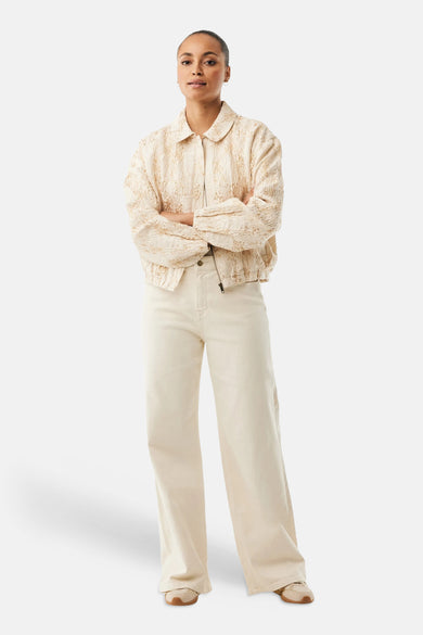 Veste courte beige de MEXX, texturée avec fermeture éclair, portée avec un pantalon crème et des baskets.
