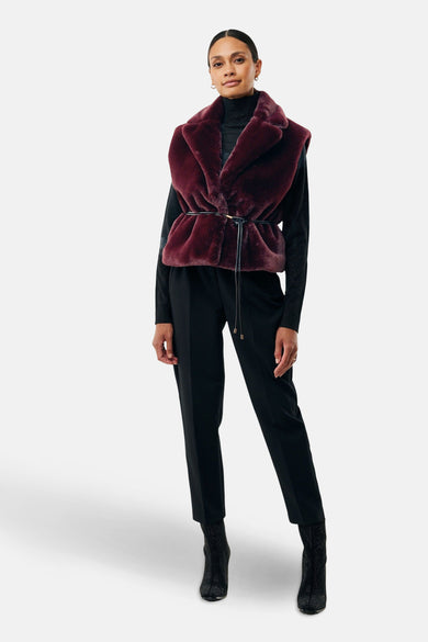 Veste sans manches bordeaux en fausse fourrure de MEXX, portée sur un pull noir et un pantalon noir.