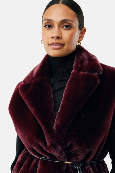 Veste sans manches bordeaux de MEXX, col large en fausse fourrure, portée sur un col roulé noir brillant.