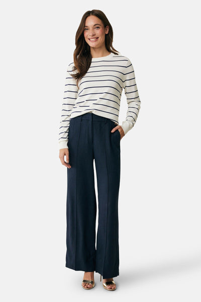 Pull à col rond écru de MEXX, à rayures horizontales bleues, porté avec un pantalon large bleu marine et des sandales dorées.