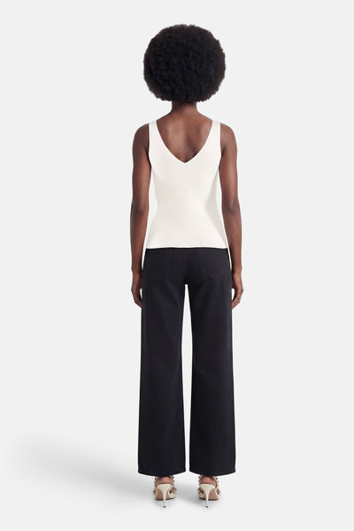 Débardeur blanc de MEXX en maille côtelée avec décolleté en V dans le dos, porté avec un pantalon large noir et des sandales à talons cloutées.