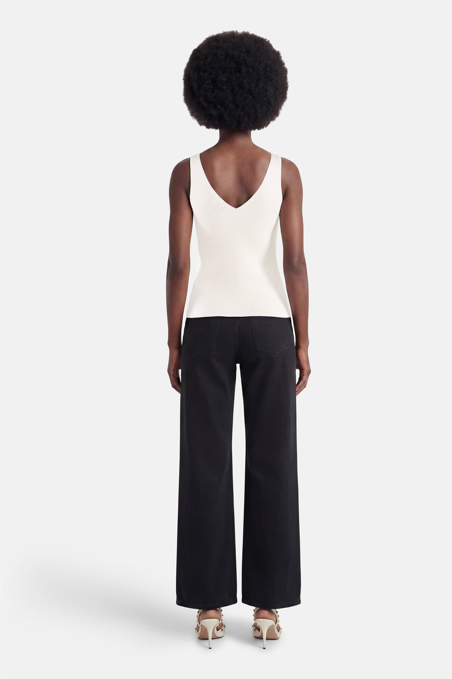 Débardeur blanc de MEXX en maille côtelée avec décolleté en V dans le dos, porté avec un pantalon large noir et des sandales à talons cloutées.
