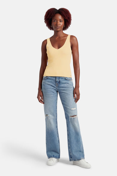 Débardeur jaune à col en V par MEXX, porté avec un jean bleu déchiré et des baskets blanches.