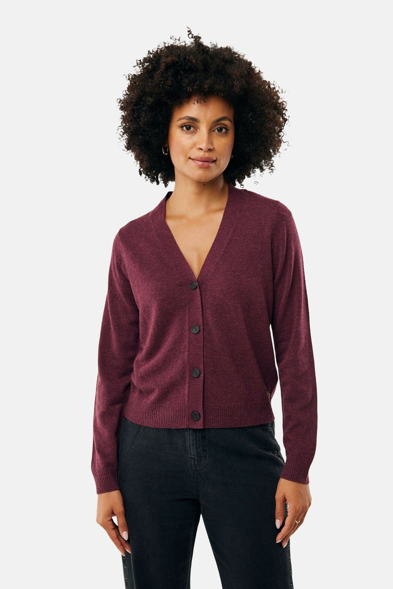 Bordeaux fijngebreid vest van MEXX, gedragen met een zwarte broek met knopen aan de zijkant.
