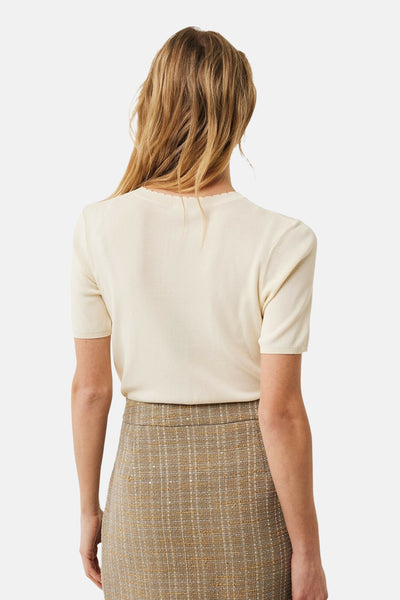Pull à col rond écru de MEXX, avec une bordure festonnée et porté avec une jupe à carreaux texturée.
