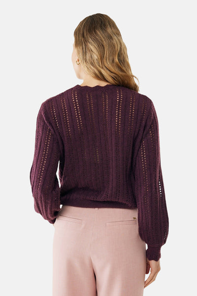 Pull bordeaux à col rond de MEXX, avec des motifs ajourés verticaux, porté avec un pantalon rose.
