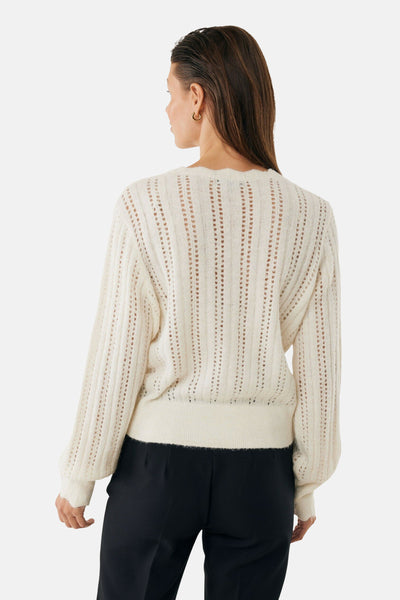 Cardigan écru en maille ajourée de MEXX, manches longues bouffantes et porté avec un pantalon noir.