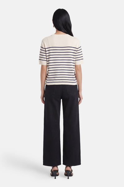 Pull col O écru à rayures marines de MEXX, manches courtes, vu de dos avec un pantalon noir large et des sandales.