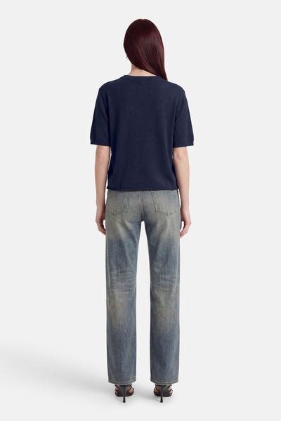 Pull col O bleu marine à manches courtes de MEXX, porté de dos avec un jean délavé et des talons.