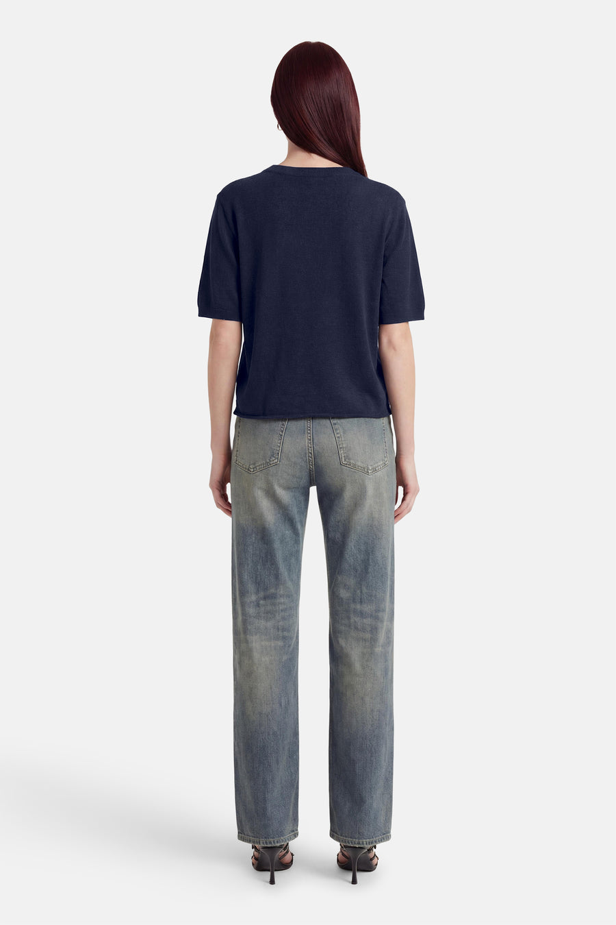 Pull col O bleu marine à manches courtes de MEXX, porté de dos avec un jean délavé et des talons.