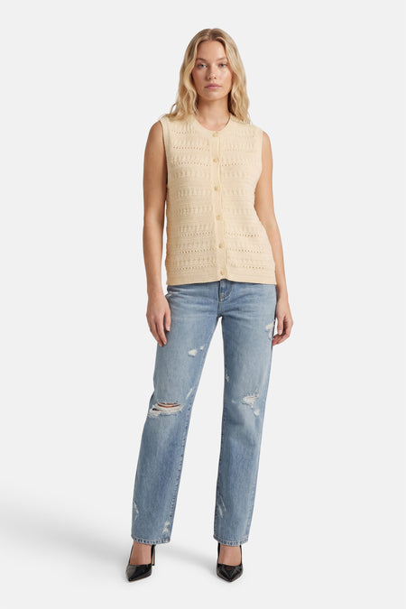 Blouse beige sans manches de MEXX, en crochet, portée avec un jean déchiré et des escarpins noirs.