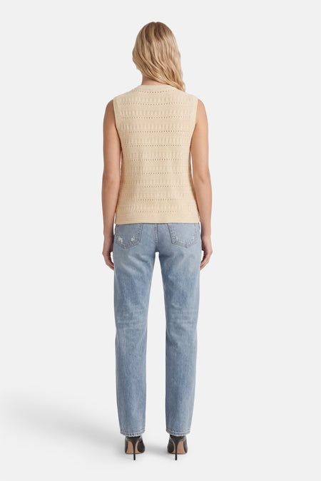 Chemisier sans manches beige de MEXX, avec un motif ajouré texturé, porté avec un jean bleu clair et des talons noirs.