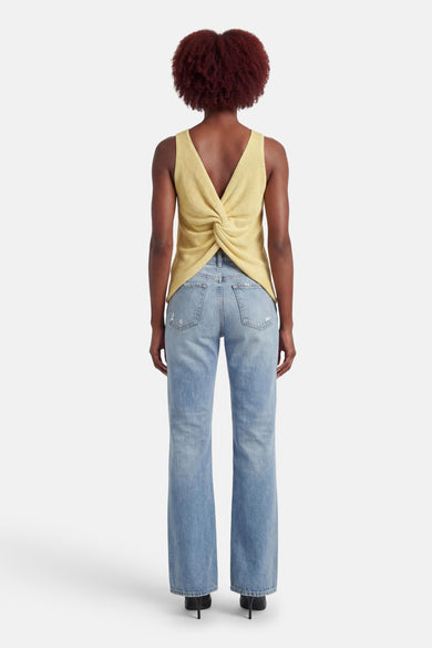 Débardeur jaune de MEXX, avec un dos torsadé, porté avec un jean taille haute et des talons noirs.