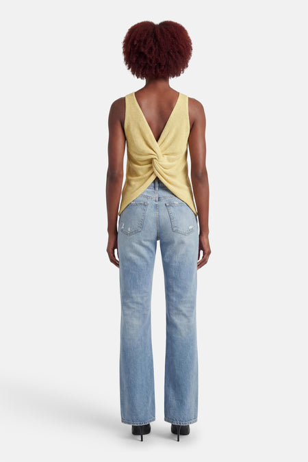 Débardeur jaune de MEXX, avec un dos torsadé, porté avec un jean taille haute et des talons noirs.