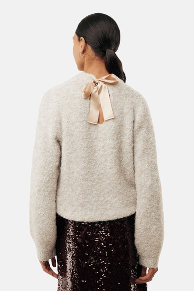 Pull écru à col rond de MEXX, agrémenté d'un nœud décoratif en satin au dos, porté avec une jupe à paillettes.
