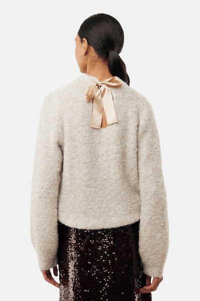 Pull écru à col rond de MEXX, agrémenté d'un nœud décoratif en satin au dos, porté avec une jupe à paillettes.

