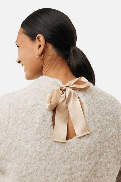 Pull à col rond écru de MEXX, agrémenté d'un nœud décoratif au dos et porté avec des boucles d'oreilles dorées.