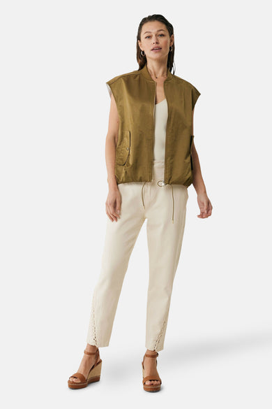 Veste kaki sans manches de MEXX, portée sur un débardeur blanc et un pantalon beige à lacets.