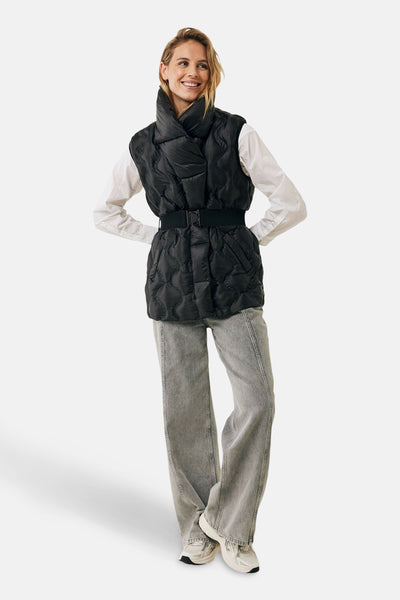 Veste courte noire de Mexx, matelassée avec ceinture noire, portée avec une chemise blanche et un jean gris.
