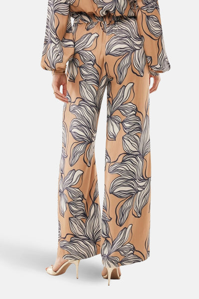 Pantalon ample multicolore de MEXX, motif floral en beige et blanc, porté avec des chaussures à talons dorées.