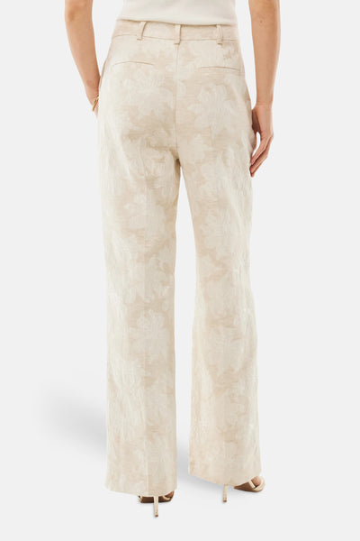 Pantalon beige de MEXX, coupe droite, à motif floral texturé, porté avec un haut et des escarpins.
