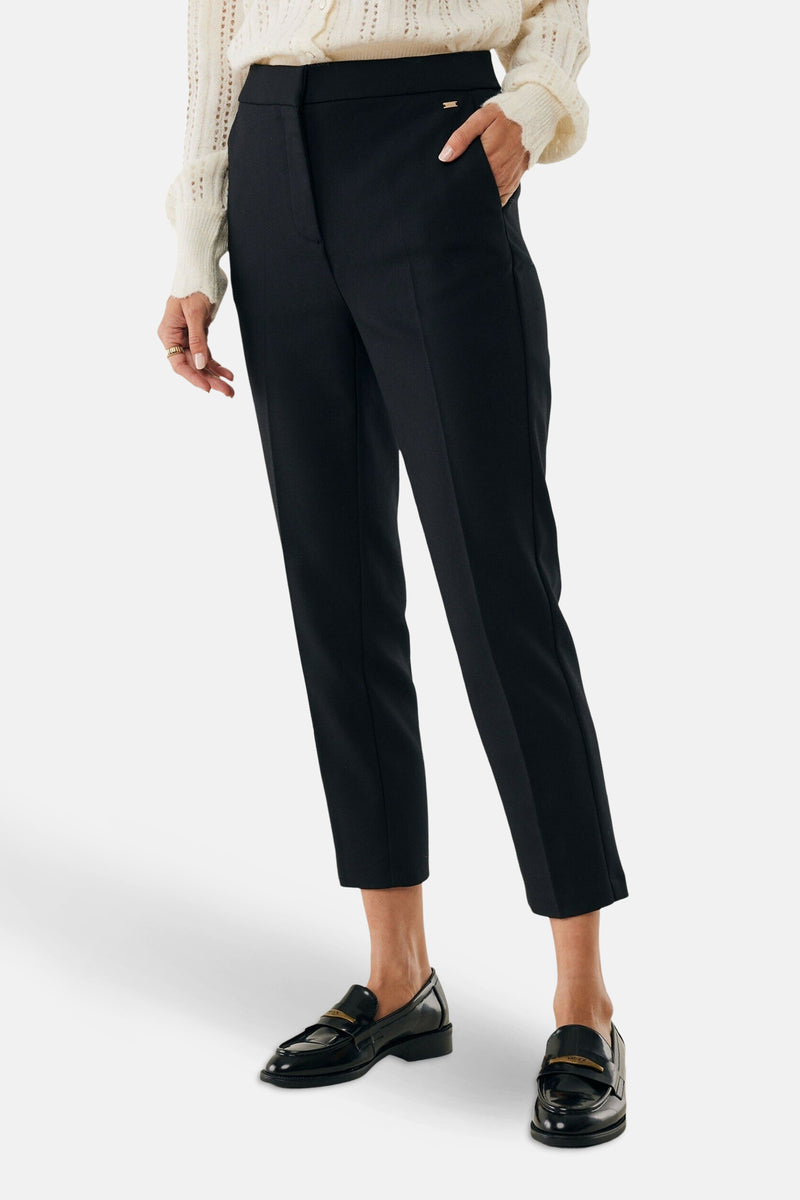 Pantalon chino 7/8 noir de MEXX, porté avec des mocassins noirs vernis et un pull en maille ajourée.
