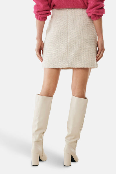 Jupe courte écru de MEXX, texturée en tweed, portée avec des bottes hautes crème.