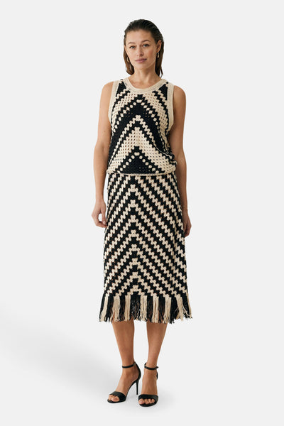 Jupe 3/4 noire en crochet de MEXX, avec motif géométrique et détails de franges, portée avec des sandales à talons.
