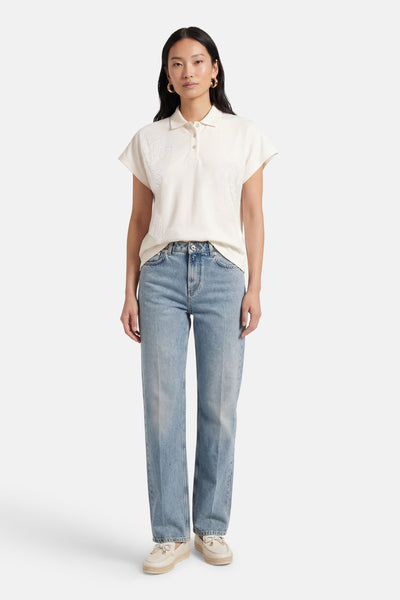 T-shirt blanc de MEXX, avec broderie décorative sur les épaules, porté avec un jean bleu et des chaussures beiges.
