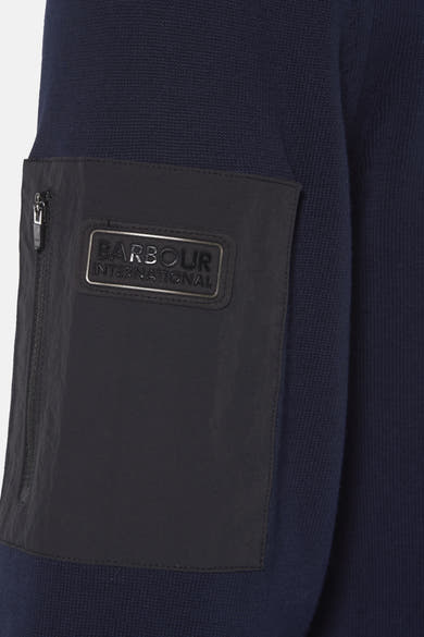 Barbour blauwe coltrui, met een zwarte zak met rits en een rechthoekig metalen logo.