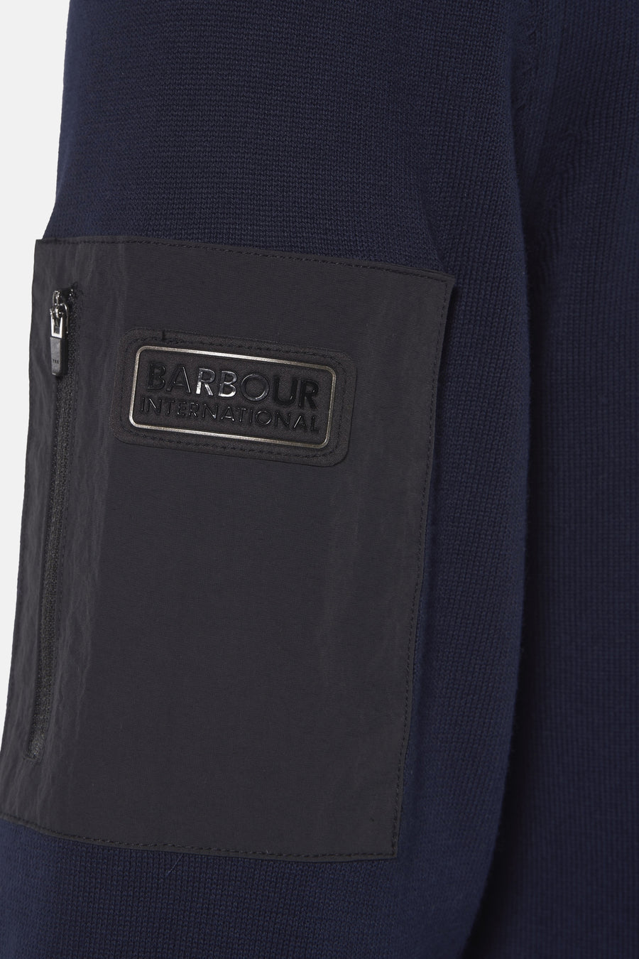 Barbour blauwe coltrui, met een zwarte zak met rits en een rechthoekig metalen logo.