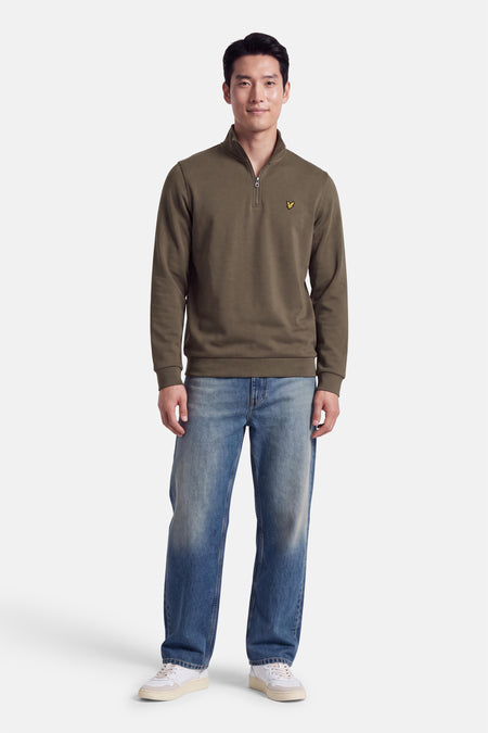 Sweat à col roulant kaki par LYLE & SCOTT, avec logo jaune sur poitrine, porté avec jeans bleus et baskets blanches, vue de face.