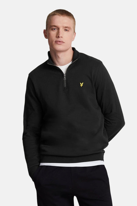 Sweat noir zippé à col montant de Lyle & Scott, avec logo brodé sur la poitrine, porté avec un t-shirt blanc.