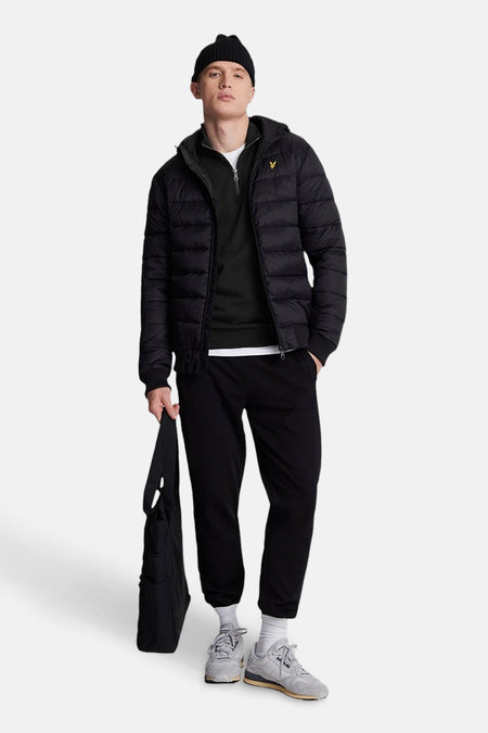 Sweat noir par LYLE & SCOTT, porté avec un bonnet noir, un blouson matelassé et un pantalon noir.