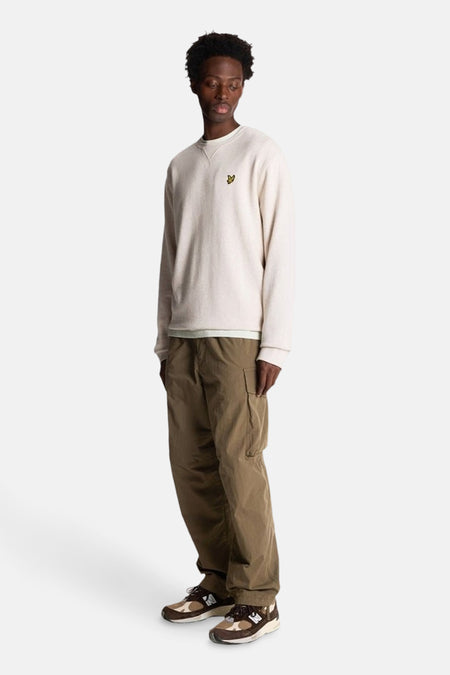Beige sweater met ronde hals van LYLE & SCOTT, gedragen met een olijfgroene cargobroek en bruine sneakers.