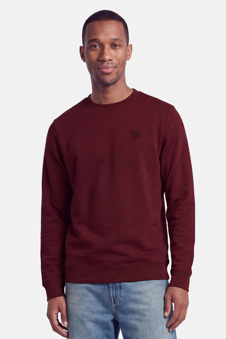 Sweat col O bordeaux de LYLE & SCOTT, coupe classique, logo brodé discret sur poitrine, porté avec jeans délavés, vue frontale.