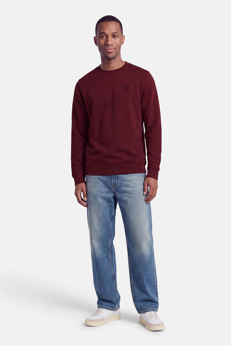 Sweat col O bordeaux de LYLE & SCOTT, coupe classique, logo brodé sur poitrine, porté avec jeans délavés et baskets blanches, vue frontale.