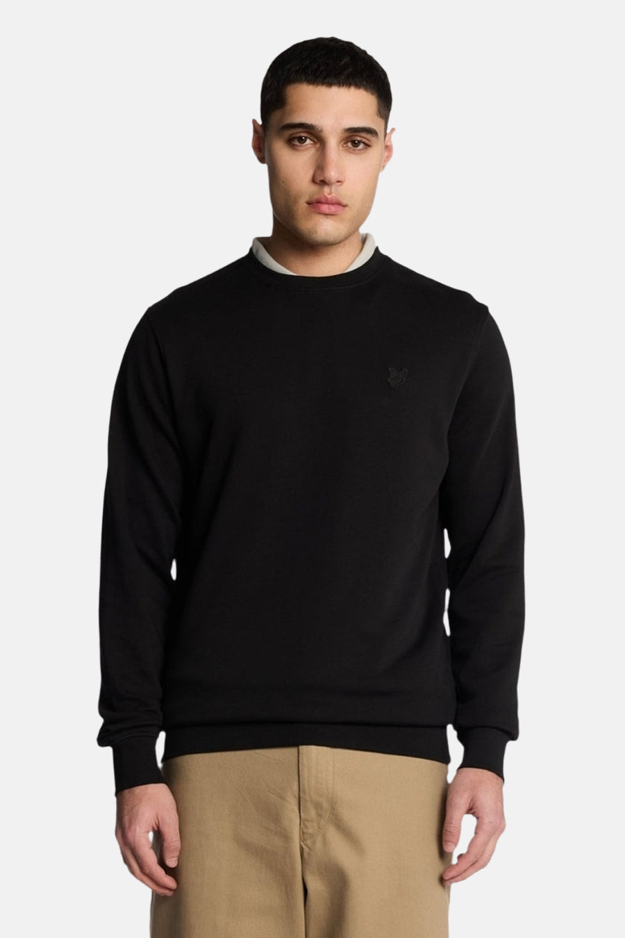 Black crewneck sweatshirt with ribbed cuffs and hem, featuring small embroidered logo on chest, worn by model in front view.