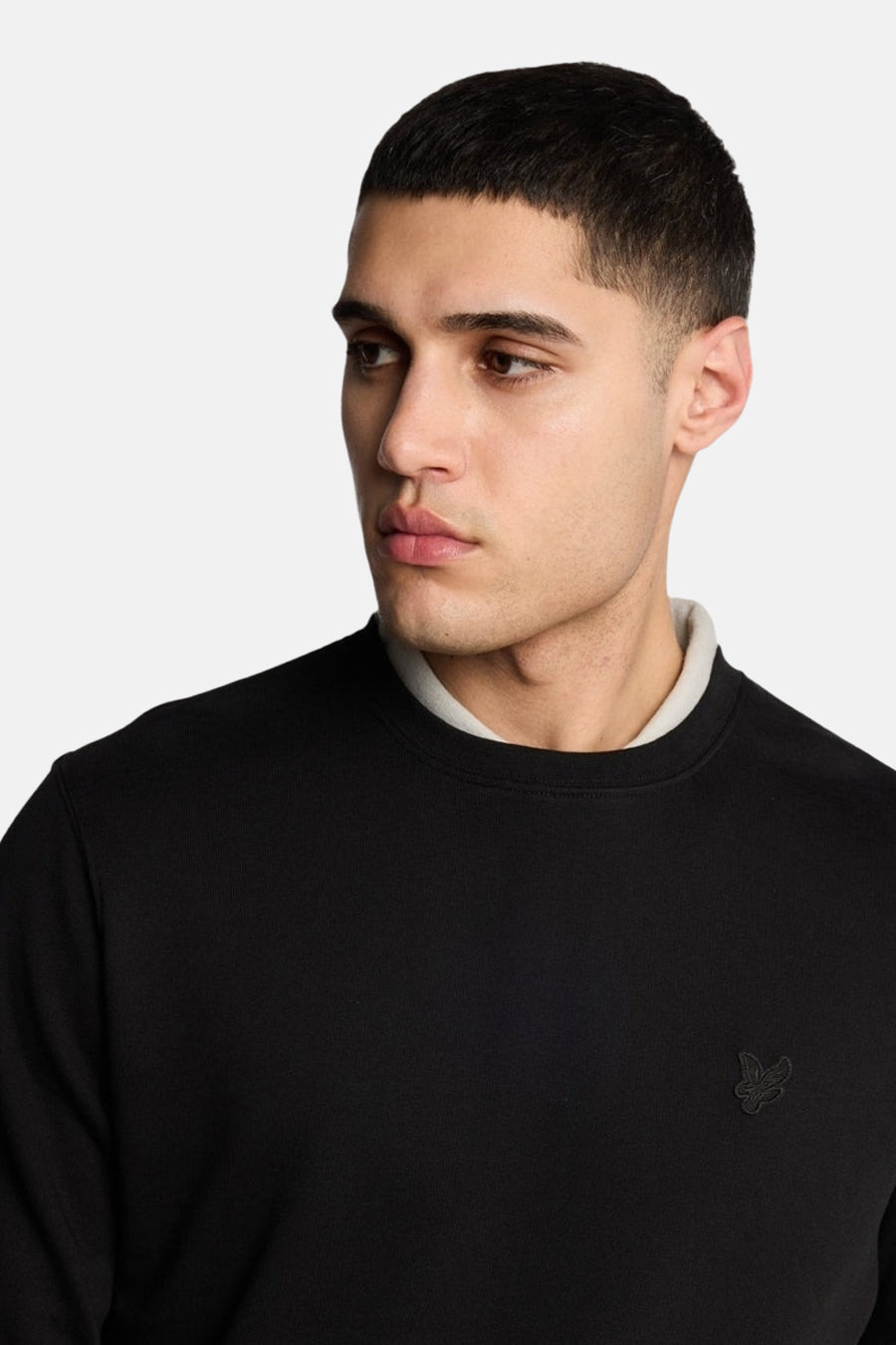 Black crewneck sweatshirt with light gray ribbed collar and small embroidered logo on chest, worn by model in side view.