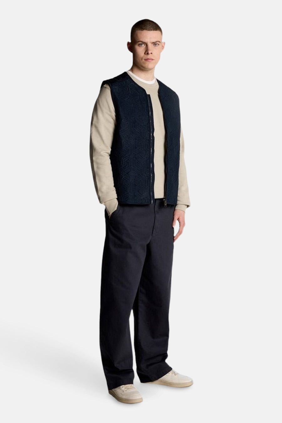 Sweat-shirt gris de Lyle & Scott, porté avec un gilet bleu marine à motif géométrique, un pantalon ample et des chaussures claires.