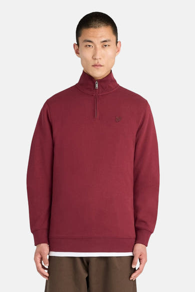Burgundy half-zip sweatshirt with ribbed cuffs and hem, featuring small embroidered logo on chest, front view on model wearing white tee and brown pants