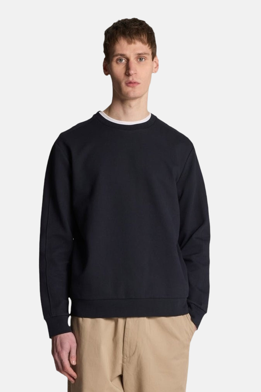 Sweat bleu de LYLE & SCOTT, avec un col rond et des manches longues, porté avec un pantalon beige.