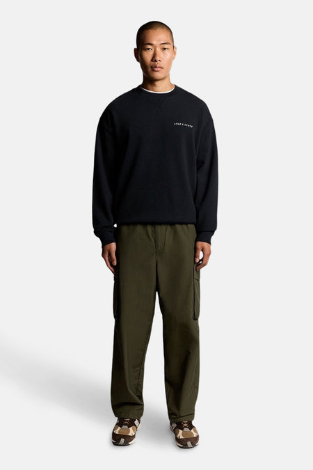 Donkerblauwe sweater van LYLE & SCOTT, gedragen met een olijfgroene cargobroek en sneakers met patroon.