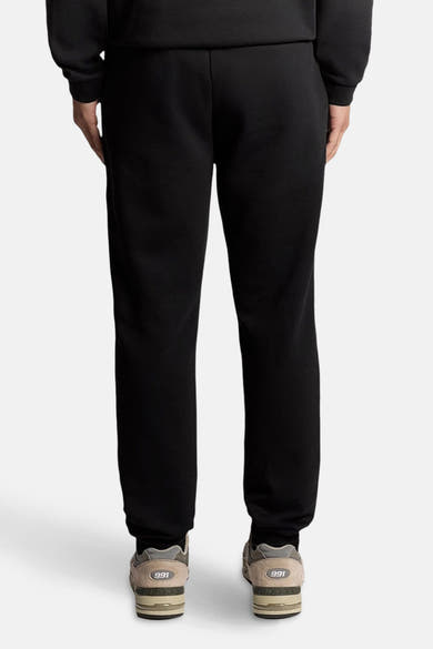 Zwarte joggingbroek van LYLE & SCOTT, gedragen met neutrale sneakers met dikke zolen, achterzijde.