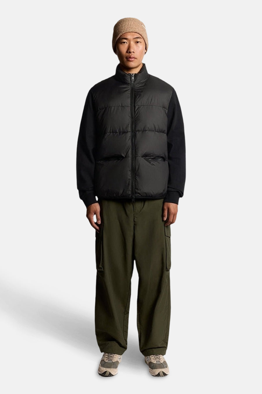 Veste de pluie noire par LYLE & SCOTT, portée avec un bonnet beige et un pantalon cargo vert olive.