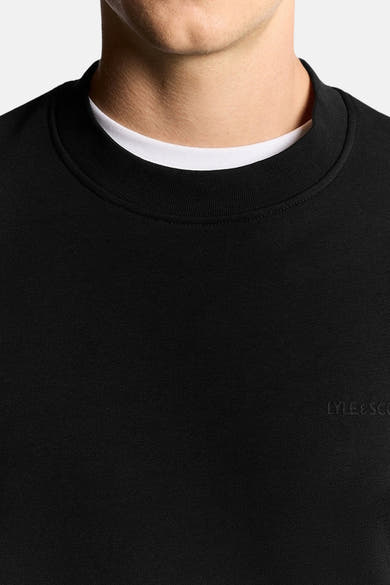 Sweat-shirt noir à col rond de LYLE & SCOTT, porté sur un t-shirt blanc, en tissu texturé.