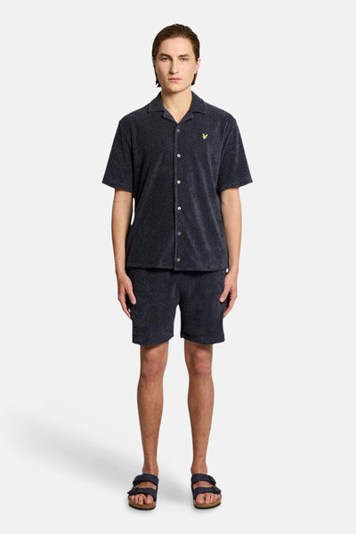 Short bleu de LYLE & SCOTT, porté avec une chemise assortie et des sandales.