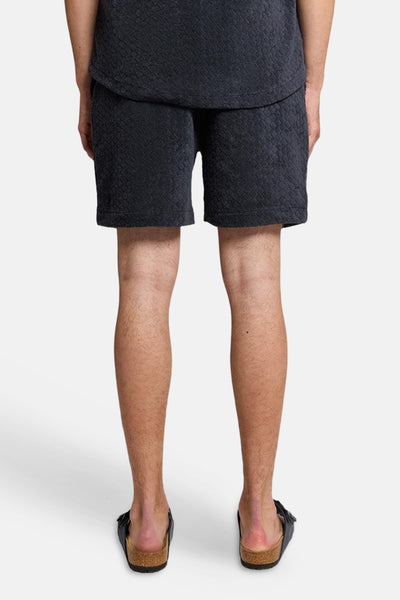 Short bleu de LYLE & SCOTT, texture nid d'abeille, porté avec des sandales de couleur foncée, vue de dos.
