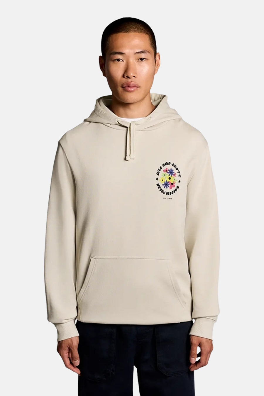 Sweat à capuche écru de LYLE & SCOTT avec un motif floral coloré sur la poitrine et une poche kangourou, porté par un homme.