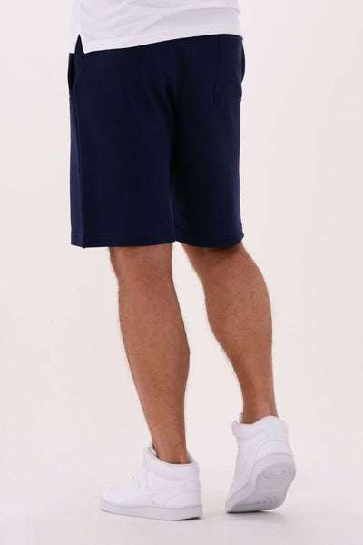 Korte blauwe LYLE & SCOTT, gedragen met een wit T-shirt en witte hoge sneakers.